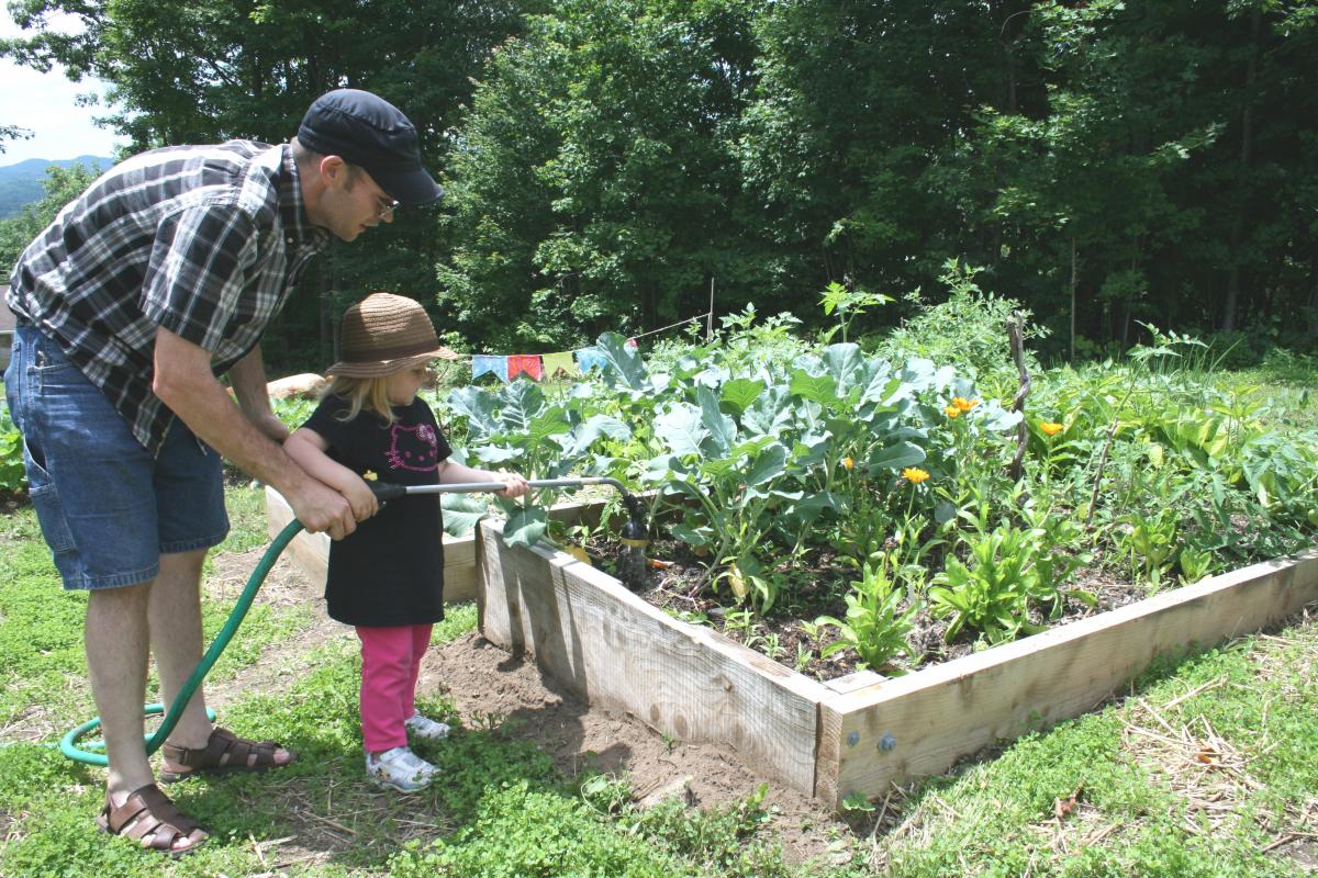 Gardener and child watering vibrant garden bed