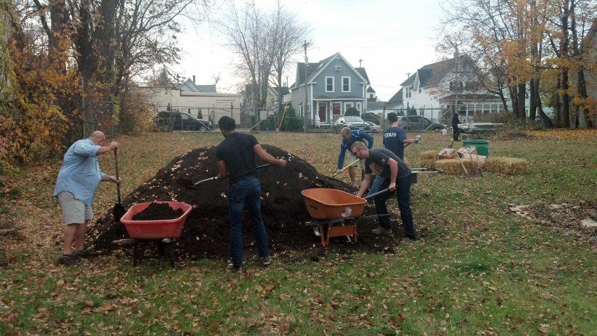 people working with shovels and wheelbarrows to spread pile of compost