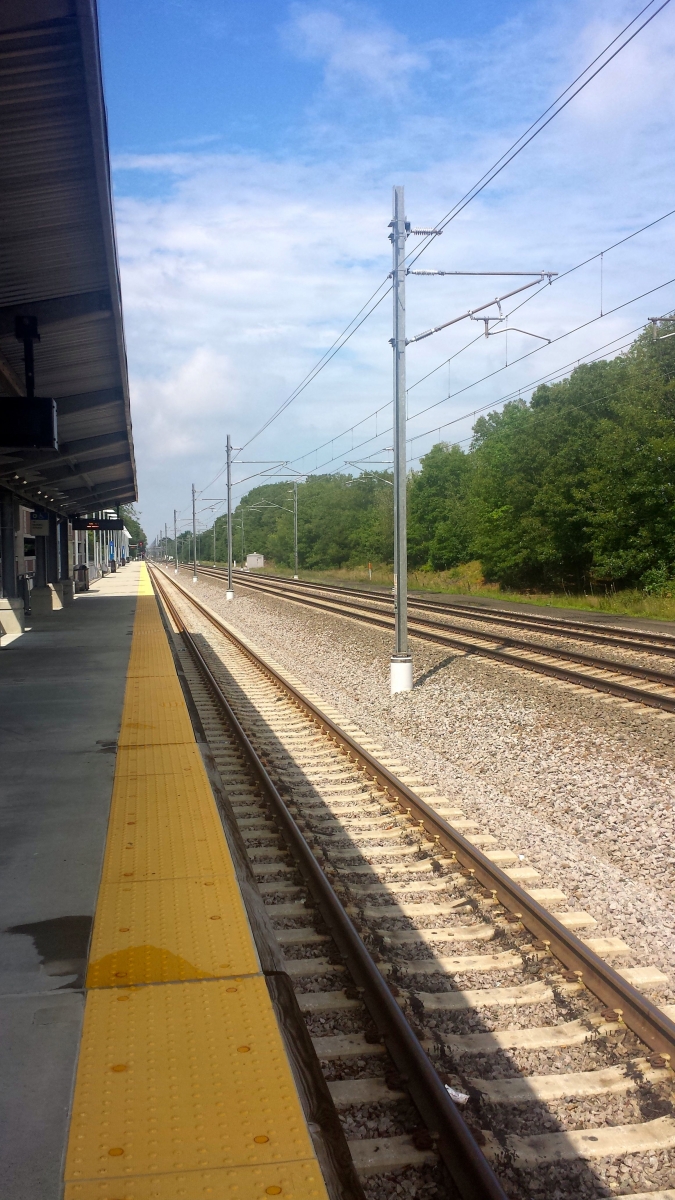 The Wickford Junction station is quiet in the early afternoon. Beyond the trees next to the tracks are residential areas. Taken by Randall, 2016